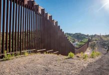 Trump Deploys Troops—Mexico Border Erupts Tall metal border wall with rural landscape