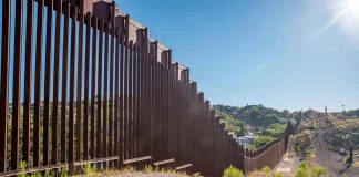 Tall metal border wall with rural landscape