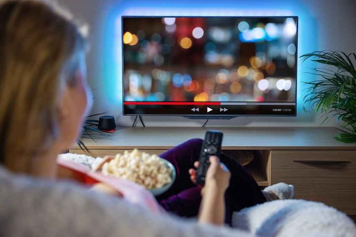 Person sitting on a couch watching a movie on a TV with popcorn in hand