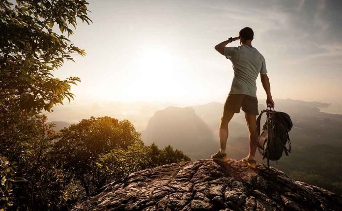 shutterstock_239978665.jpg Hiker standing on a rocky outcrop overlooking a valley at sunset