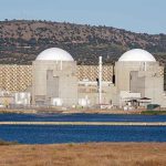 Nuclear power plant with domed structures beside a water body and mountains in the background