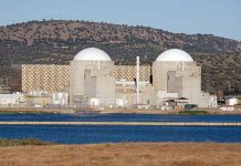 Nuclear power plant with domed structures beside a water body and mountains in the background