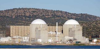 Nuclear power plant with domed structures beside a water body and mountains in the background