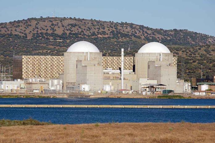 Nuclear power plant with domed structures beside a water body and mountains in the background