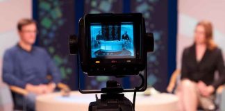 Camera focused on a television studio interview with two seated hosts