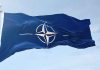NATO flag waving against blue sky.