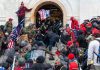 Crowd storming a building entrance with flags and signs.