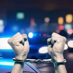 Horrific Park Attack Exposes Open-Borders Chaos Hands in handcuffs in front of police cars.