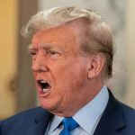 Man in suit with open mouth, speaking passionately.