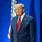 Man in suit next to American flag.