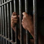 Hands gripping prison cell bars tightly.