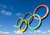 Olympic Hero Turned MOST WANTED Drug Lord Olympic rings sculpture against blue sky.