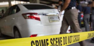 Crime scene tape blocking off white sedan.