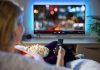 Person sitting on a couch watching a movie on a TV with popcorn in hand