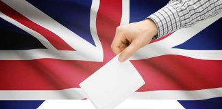 A hand placing a ballot into a white ballot box with the British flag in the background