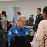 Cash, Terror, and U.S. Airports TSA agent checks passengers documents at airport security.