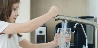 Girl filling glass with water from kitchen faucet.