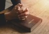 Hands praying on a Bible.