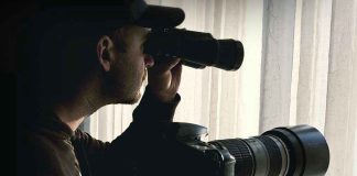Person looking through binoculars beside a camera.