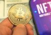 Person holding Bitcoin coin, NFT text on screen.