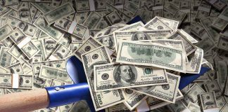 A shovel filled with stacks of cash on a background of scattered dollar bills
