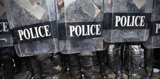 Police officers in riot gear standing behind shields marked POLICE