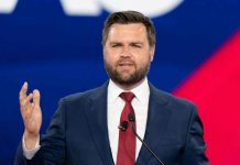 Man in a suit speaking at an event.