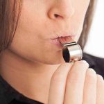 Person blowing a silver whistle close-up.