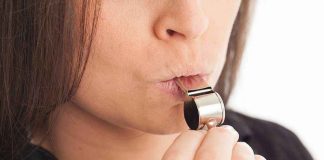 Person blowing a silver whistle close-up.