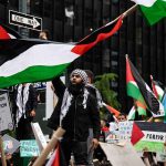 Democratic Candidate’s Explosive Terror Ties Protesters with flags and signs, one holding a megaphone.