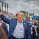 NFL Double Standard: Analyst SLAMS QB for Trump Intro Person in blue suit waving at outdoor event.