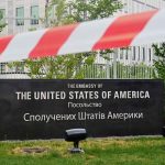 U.S. Embassy sign behind red-and-white caution tape.
