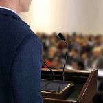 A speaker at a podium addressing an audience