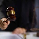 Hand holding gavel in courtroom setting.