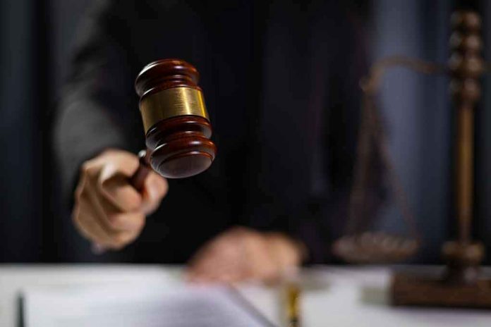 2477750649-1 Hand holding gavel in courtroom setting.