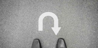 Feet in black shoes facing U-turn road marking.