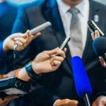 MASS SHOOTING — Developing DETAILS INSIDE Journalists holding microphones interview a person in a suit.