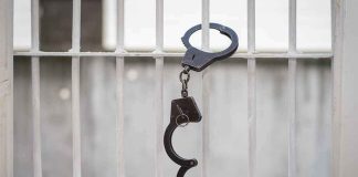 Handcuffs hanging on white metal bars.