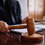 DOJ Clampdown Locks KIDS’ CARE For 20 Years A judge's hand holding a gavel in a courtroom setting