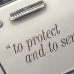 Police HQ HORROR Raises Chilling Question Close-up of a police car door with the phrase to protect and to serve
