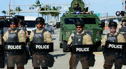 shutterstock_1751101367 Police officers in riot gear with armored vehicle behind.