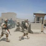 Soldiers in desert uniforms run past a checkpoint amid dust