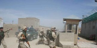 Soldiers in desert uniforms run past a checkpoint amid dust