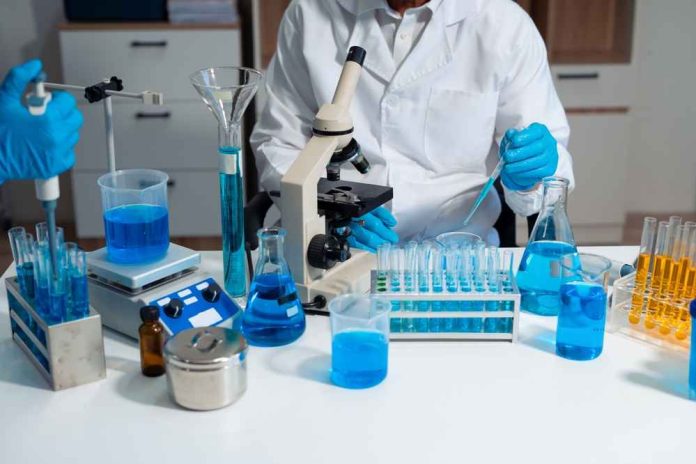 shutterstock_2664976131-1 Scientist in a lab working with blue liquids and a microscope