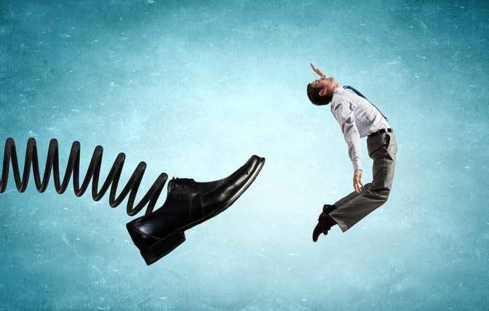 Businessman propelled backward by a giant spring-loaded shoe