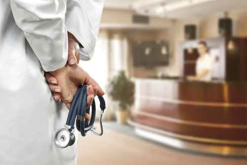 shutterstock_378847639 A doctor holding a stethoscope behind their back in a hospital reception area