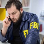 TOTALLY UNEXPECTED — FBI PROTECTED ‘Person of High Interest’ — WHY?? Man in FBI jacket talking on a phone at a desk