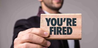 Man in suit holding a wooden sign that says You're Fired