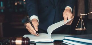 Lawyer signing documents at a desk with gavel and scales