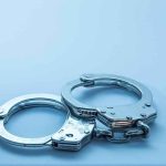 Resurfaced Police File EXPLODES on SENATE CONTENDER Metal handcuffs on a light blue surface